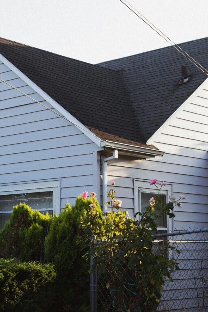 Side view of a white house with a dark roof and greenery.