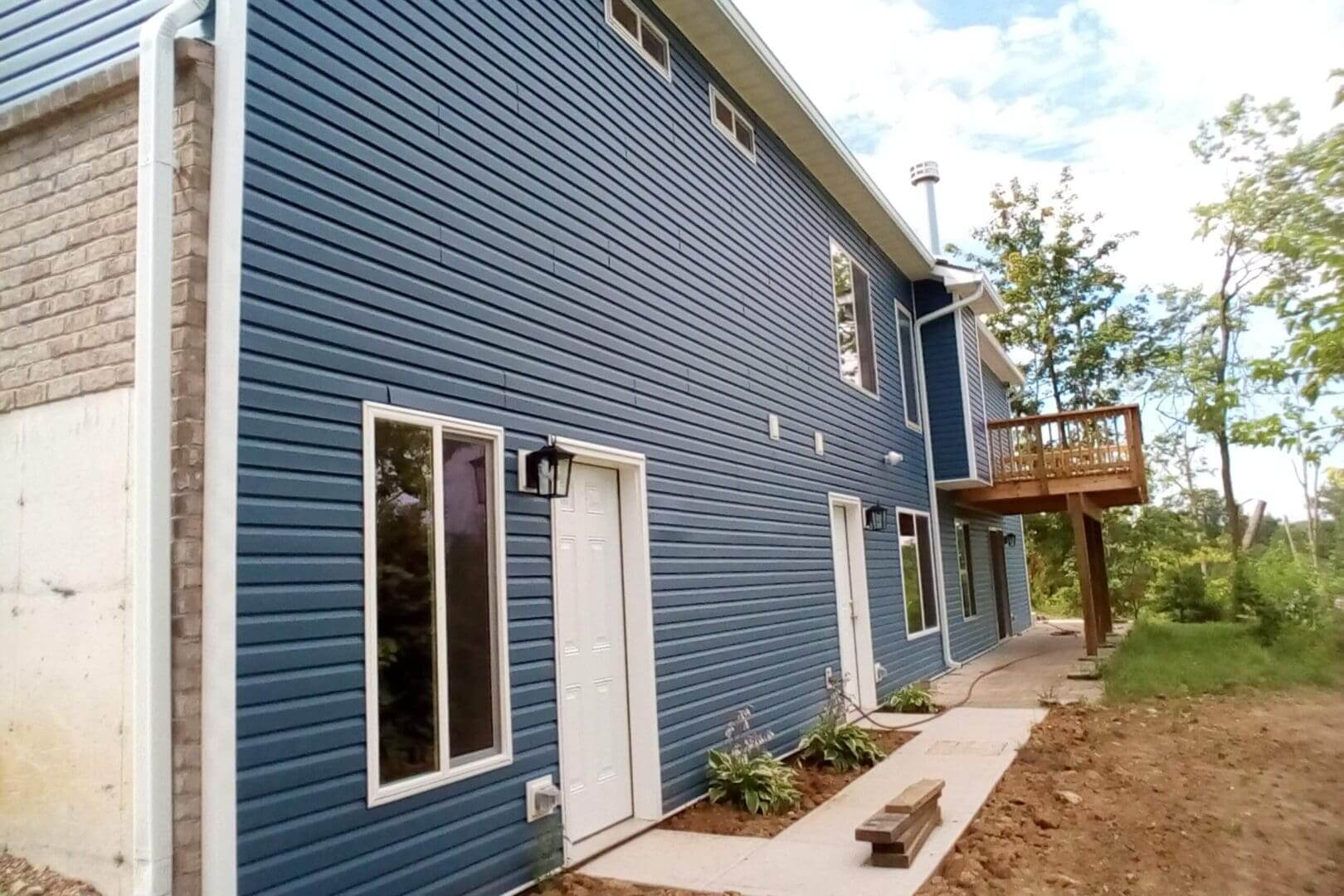 Blue house with wooden deck and windows.
