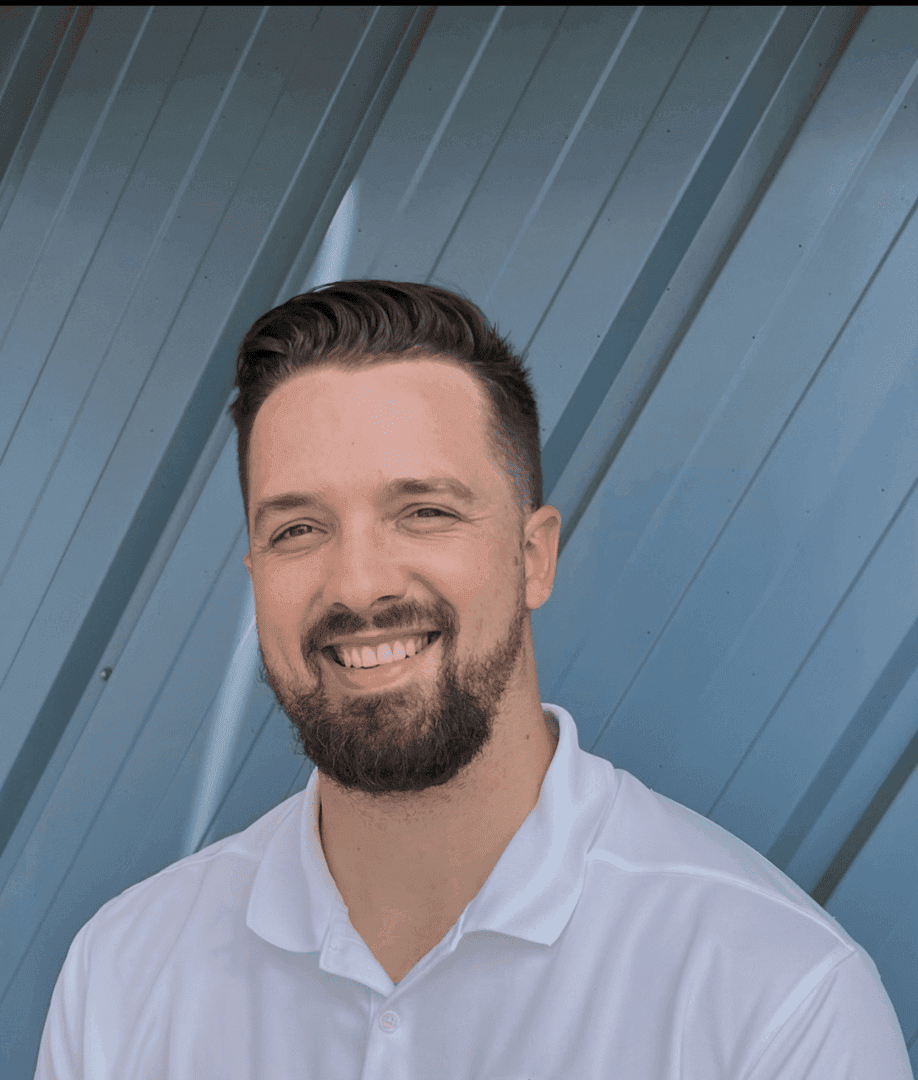 Smiling man with beard in white shirt against a geometric blue background.